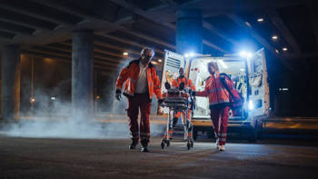 Τρία μέλη του ΕΚΑΒ μεταφέρουν έναν άνθρωπο σε φορτίο από το ασθενοφόρο